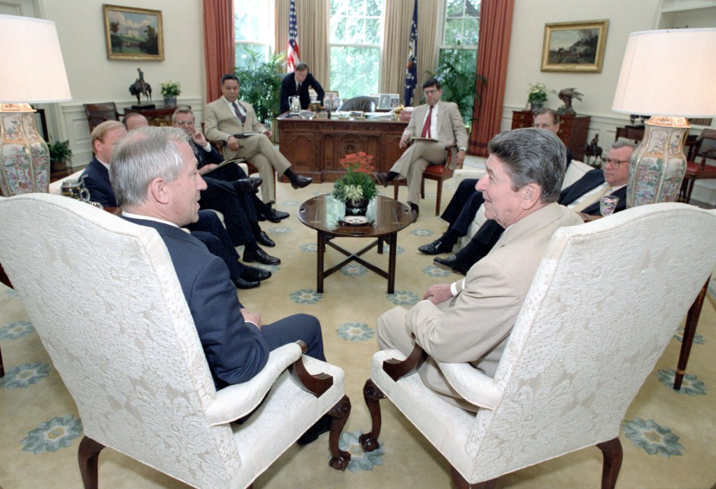 Gordievsky and Reagan in forground.  From left to right: unknown, unknown, Carlucci, Lieutenant General Colin Powell, James Kuhn (?) over desk, Deputy Chief of Staff Ken Duberstein, unknown, and Baker.
